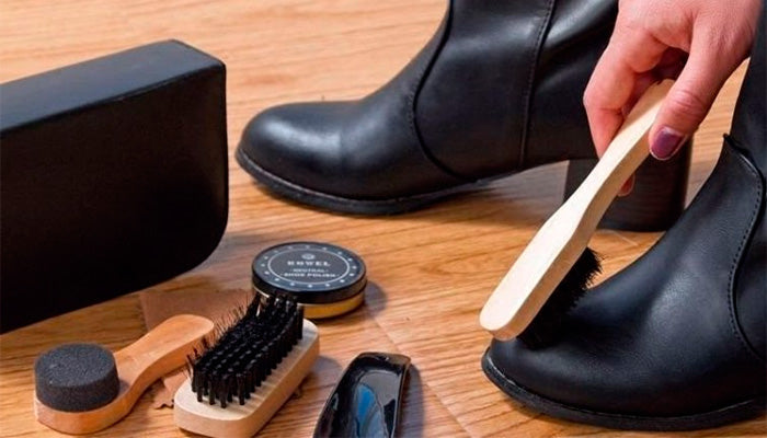 productos de limpieza de zapatos y mano con cepillo limpiando botas negras