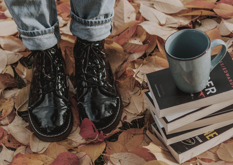 botín de charol negro sobre hojas secas y taza de café sobre libros